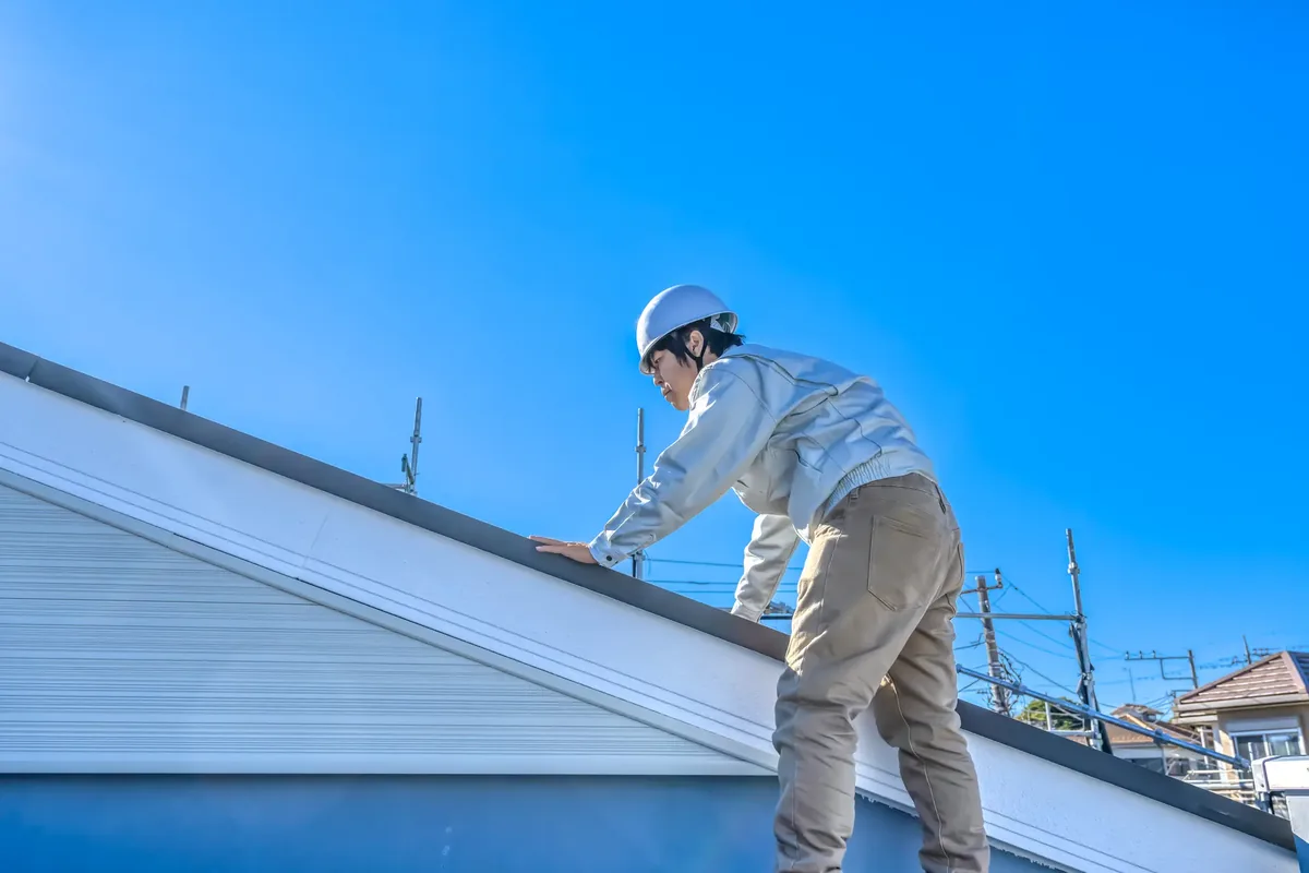 戸建て住宅の屋根に上がって修理・点検を行う職人